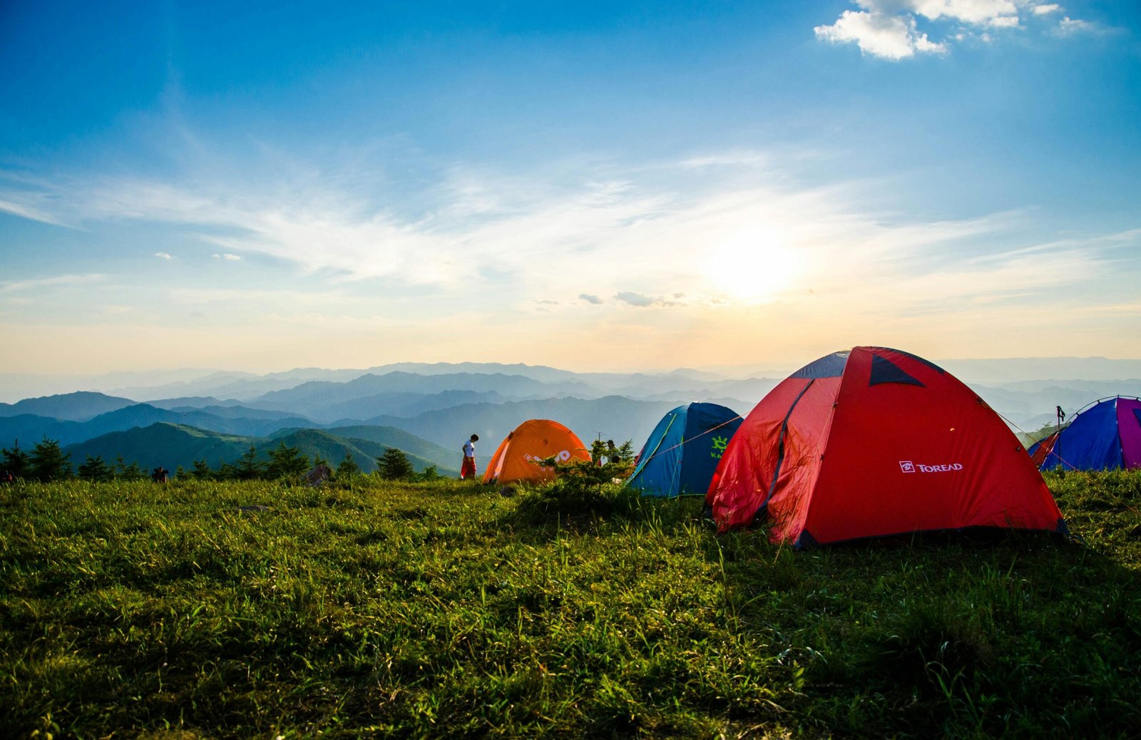 Vibrant tents on a grassy mountain ridge with a stunning sunrise view, ideal for adventure.