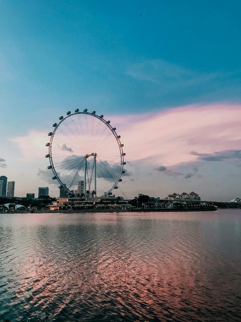 Scenic view of the Singapore Flyer and skyline at sunset reflected on water.