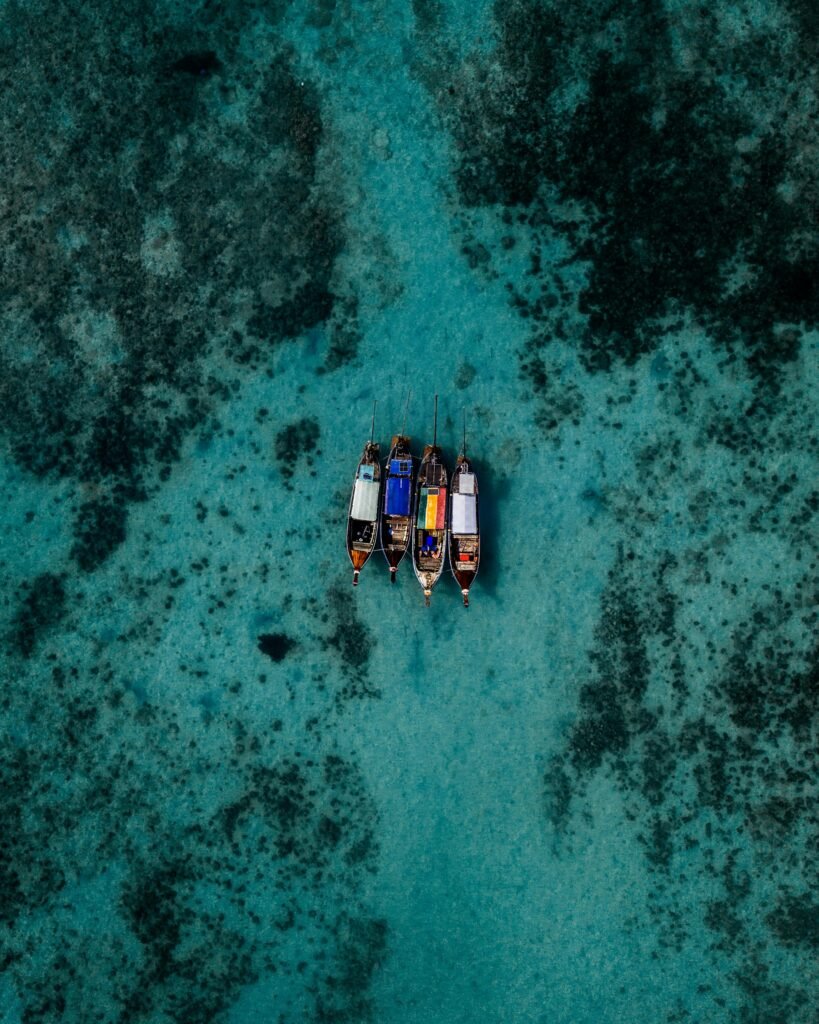 Four small boats anchored in clear turquoise waters of Thailand's sea, captured from above.