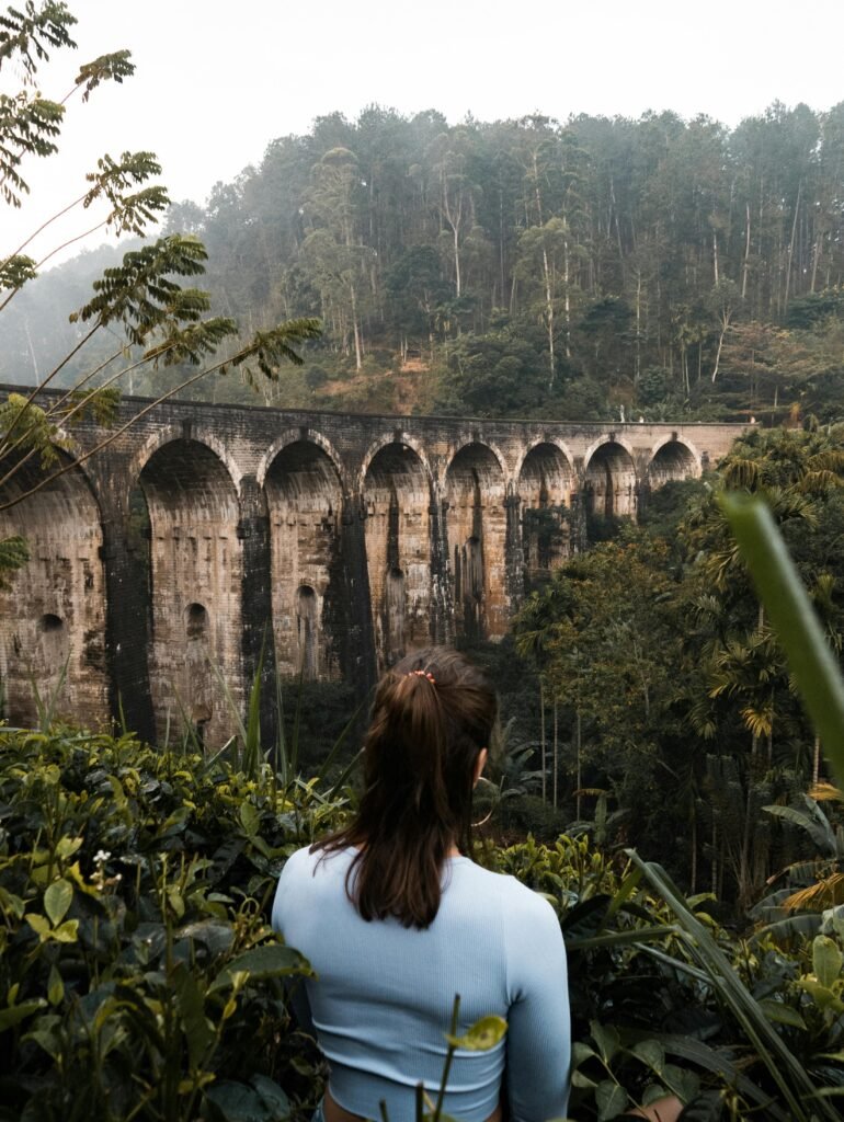 Explore the lush jungle surrounding the iconic Nine Arches Bridge in Ella, Sri Lanka, with a serene back view of a woman.