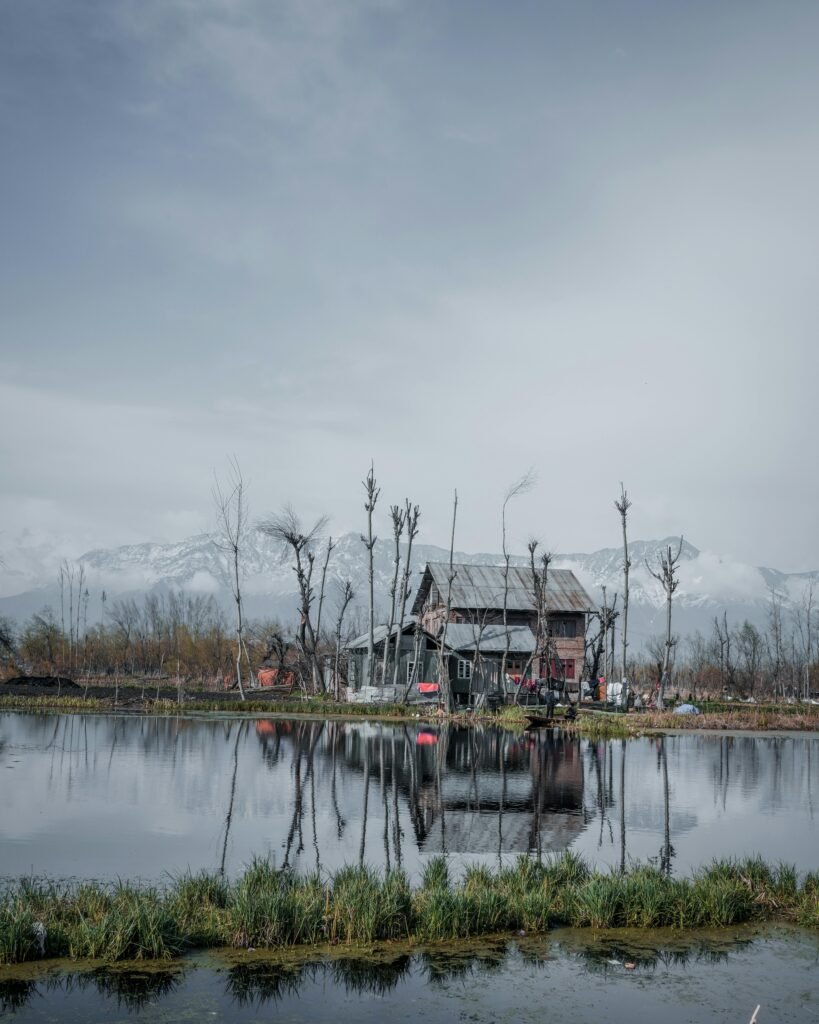 A tranquil scene of a house by a reflective lake with snow-covered mountains in Kashmir.